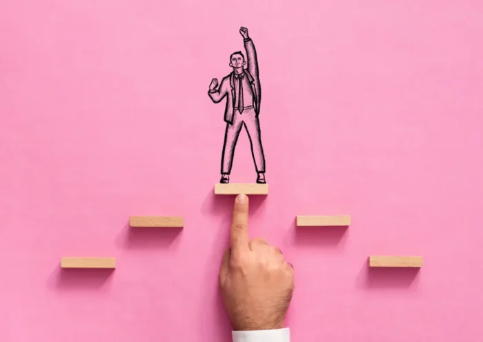 Illustration de la progression professionnelle : un manager soutient un collaborateur sur une plateforme en bois, symbolisant l'accompagnement RH et l'amélioration de la performance au travail.